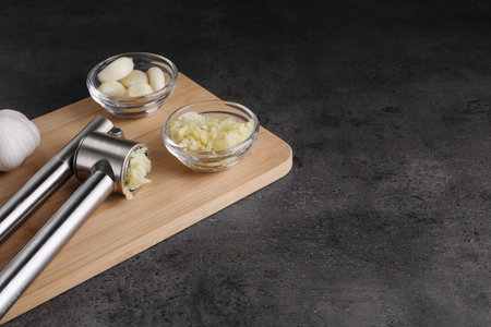 Garlic press, cloves and mince on gray table. Space for text
