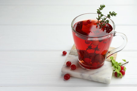 Tasty hot cranberry tea with thyme and fresh berries in glass cup on white wooden tableの写真素材
