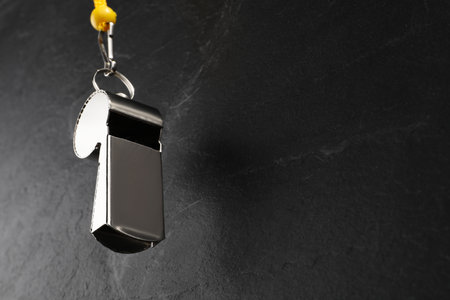Referee equipment. Metal whistle on black textured background, closeup and space for text