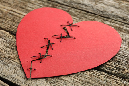 Broken heart. Torn red paper heart sewed with thread on wooden table, closeupの写真素材