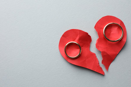 Broken heart. Halves of torn red paper heart and wedding rings on white background, top view. Space for textの写真素材