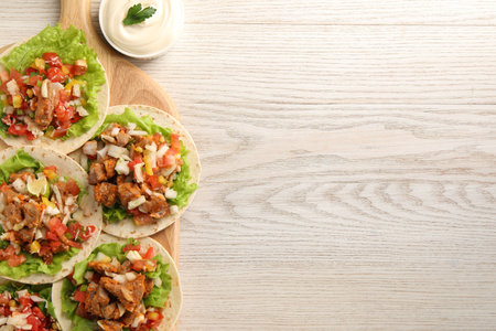 Delicious tacos with vegetables, meat and sauce on white wooden table, top view. Space for textの写真素材
