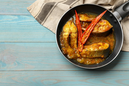 Tasty fish curry in frying pan on light blue wooden table, top view. Space for text. Indian cuisineの写真素材