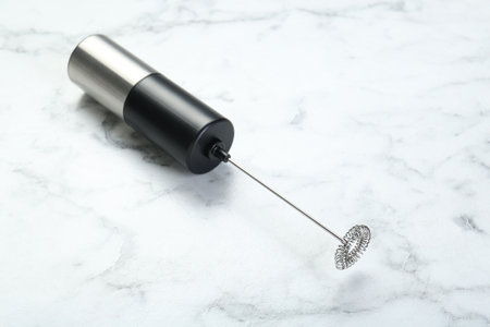 Black milk frother wand on white marble table