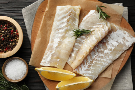 Fresh raw cod fillets, spices and lemon on wooden table, flat lay