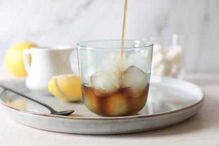 Pouring coffee into glass with ice cubes at white wooden table, closeup