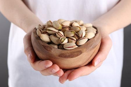 Woman holding tasty pistachios in bowl on gray background, closeupの写真素材