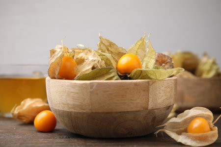 Ripe physalis fruits with calyxes in bowl on wooden table, closeupの写真素材