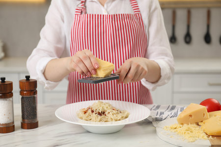 Woman grating cheese onto delicious pasta at white marble table in kitchen, closeupの写真素材