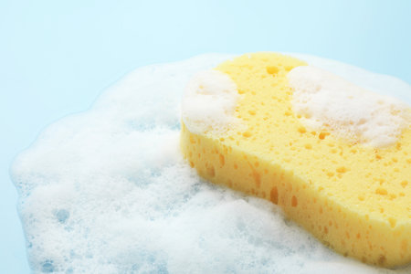 Yellow sponge with foam on light blue background, closeupの写真素材