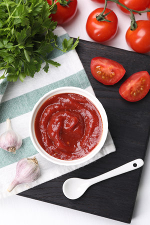 Organic ketchup in bowl, fresh tomatoes, parsley and garlic on white table, flat lay. Tomato sauceの写真素材