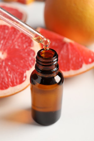 Dripping grapefruit essential oil from pipette into bottle at white table, closeupの写真素材