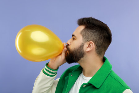 Man inflating bright balloon on violet backgroundの写真素材