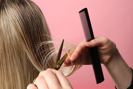 Hairdresser cutting client's hair with scissors on pink background, closeupの写真素材