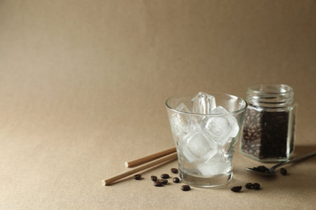 Cooking iced coffee. Ice cubes in glass, beans and straws on beige background. Space for textの写真素材