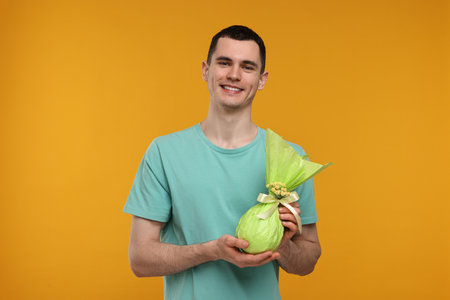 Easter celebration. Handsome young man with wrapped gift on orange background