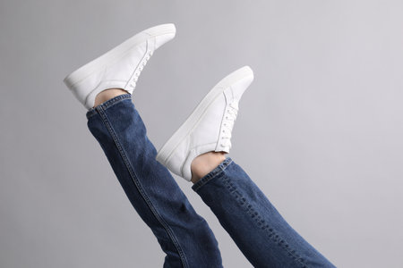 Man wearing stylish white sneakers on gray background, closeup