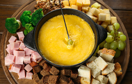 Fondue pot with melted cheese and different products on wooden table, above viewの写真素材