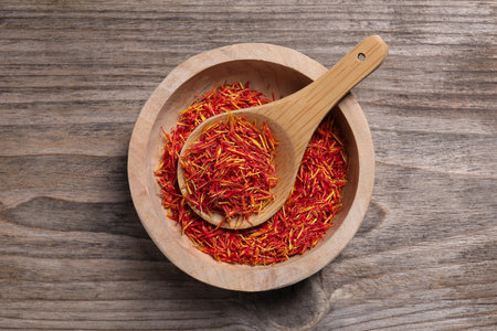 Aromatic saffron in bowl and spoon on wooden table, top viewの写真素材