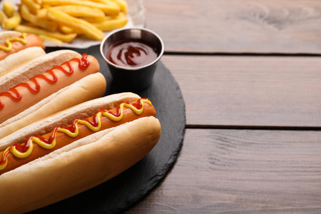 Delicious hot dogs with sauces on wooden table, closeup. Space for textの写真素材