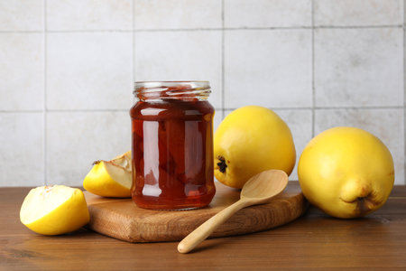Tasty homemade quince jam in jar, spoon and fruits on wooden tableの写真素材