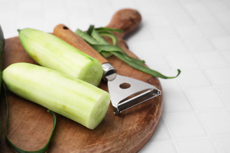 Fresh cucumbers and peeler on white tiled table, closeup. Space for textの写真素材