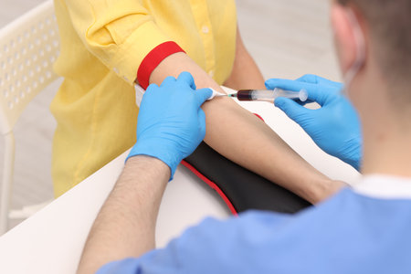 Doctor taking blood sample from patient with syringe at white table in hospital, closeupの写真素材