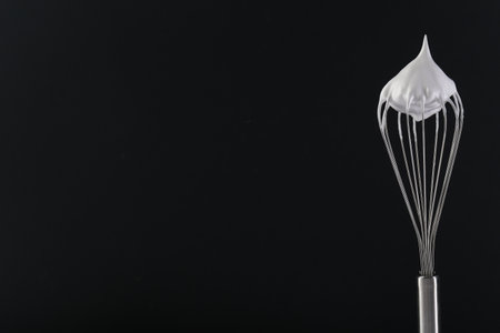 Whisk with whipped cream on black background. Space for textの写真素材