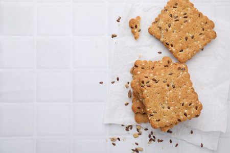 Cereal crackers with flax and sesame seeds on white tiled table, top view. Space for text