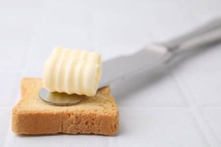 Tasty butter curl, knife and piece of dry bread on white tiled table, closeupの写真素材
