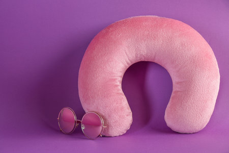 Pink travel pillow and sunglasses on violet backgroundの写真素材