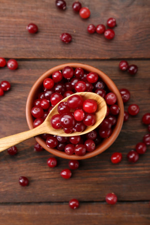 Fresh ripe cranberries in bowl and spoon on wooden table, flat layの写真素材