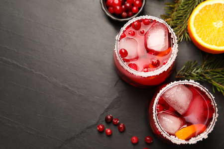 Tasty cranberry cocktail with ice cubes in glasses on dark gray textured table, flat lay. Space for textの写真素材