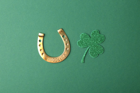 St. Patrick's day. Golden horseshoe and decorative clover leaf on green background, flat layの写真素材