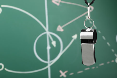 Referee whistle against green chalkboard with game scheme, closeup. Space for textの写真素材