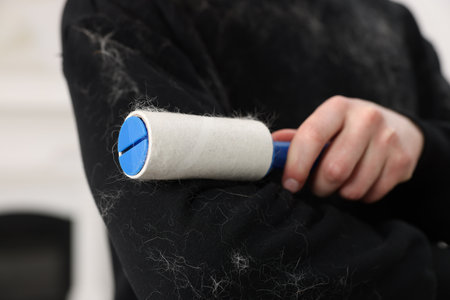 Pet shedding. Man with lint roller removing dog's hair from sweater indoors, closeupの写真素材