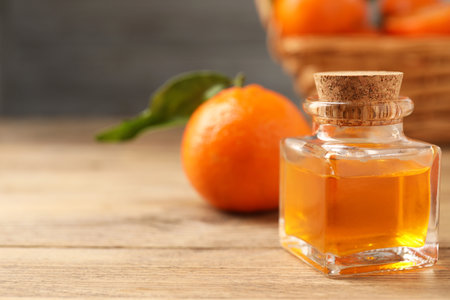 Bottle of tangerine essential oil and fresh fruit on wooden table, closeup. Space for textの写真素材