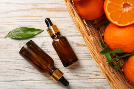 Bottle of tangerine essential oil and fresh fruits on white wooden table, flat layの写真素材