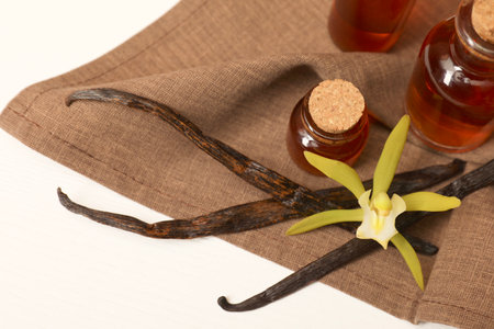Aromatic vanilla extract, pods and flower on white table, above view