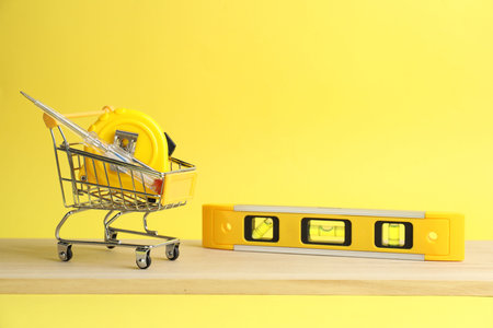 Small shopping cart and set of construction tools on yellow backgroundの写真素材
