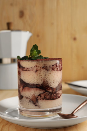 Tasty tiramisu and mint in glass on light wooden table, closeupの写真素材