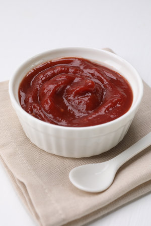 Organic ketchup in bowl and spoon on white table. Tomato sauce