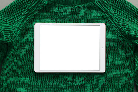 Modern tablet on green sweater, top view. Space for text