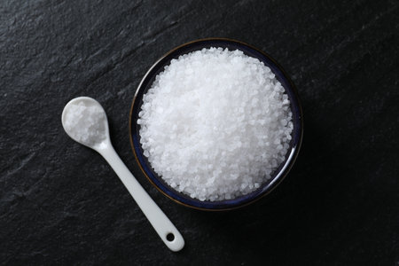 Organic white salt in bowl and spoon on black table, top viewの写真素材