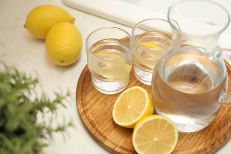 Jug, glasses with clear water and lemons on white table in kitchen, closeupの写真素材