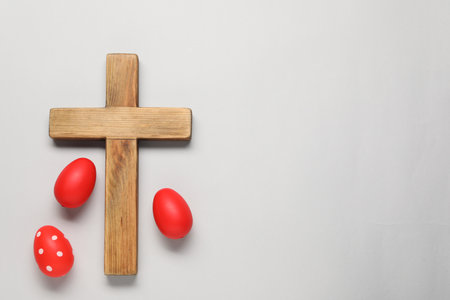 Wooden cross and painted Easter eggs on light gray background, flat lay. Space for textの写真素材