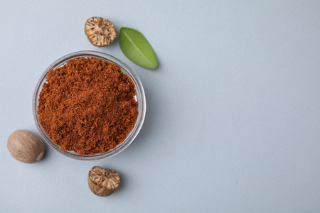 Nutmeg powder in bowl, seeds and green leaf on white background, flat lay. Space for textの写真素材