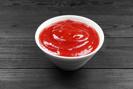 Delicious ketchup in bowl on black wooden table, closeup. Tomato sauceの写真素材