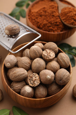 Nutmeg powder, seeds, grater and green leaves on light brown backgroundの写真素材