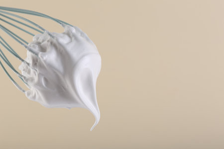 Whisk with whipped cream on beige background, closeup. Space for textの写真素材